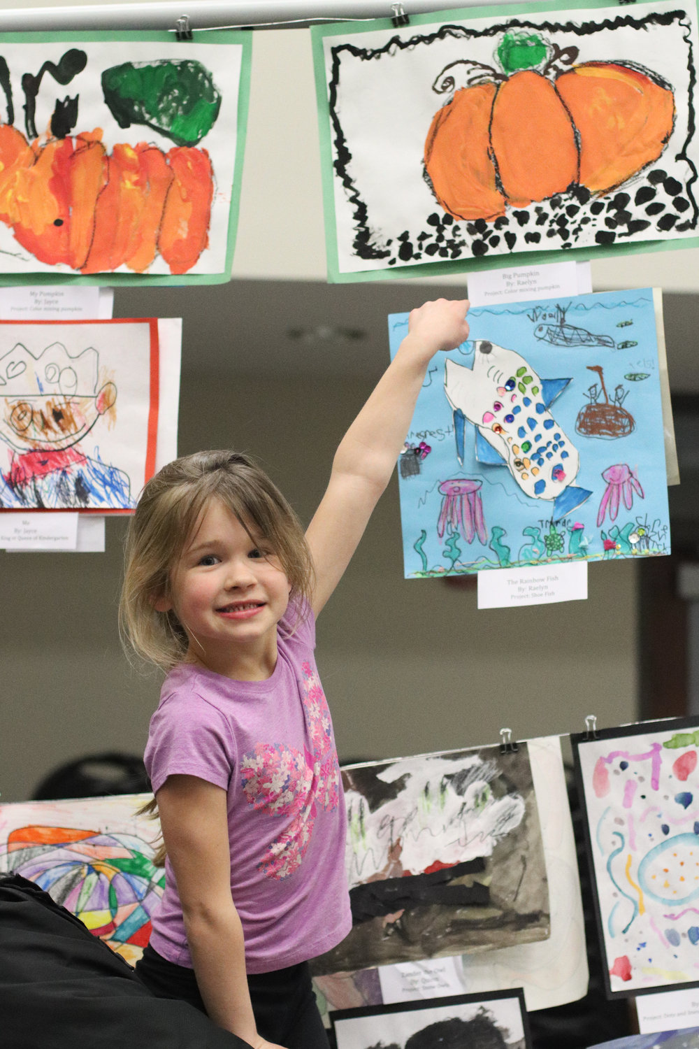 Raelyn (kindergarten) points to her project, displayed at the first annual Mid-Prairie AK-12 art show.