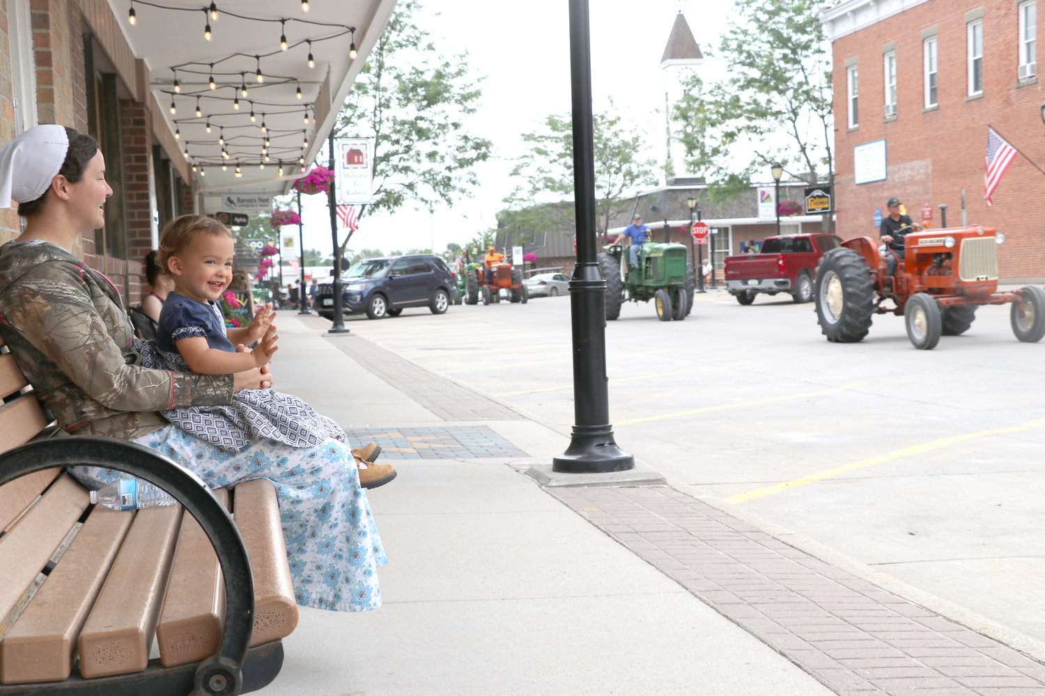 Morgan, who is almost two years old, waves to tractors with her mom, Dianne in downtown Kalona.